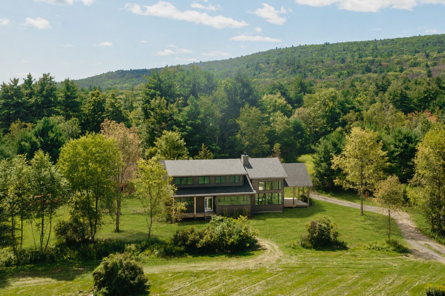 Hemlock House — aerial view of the front of the house and porches with the wooded ridge behind